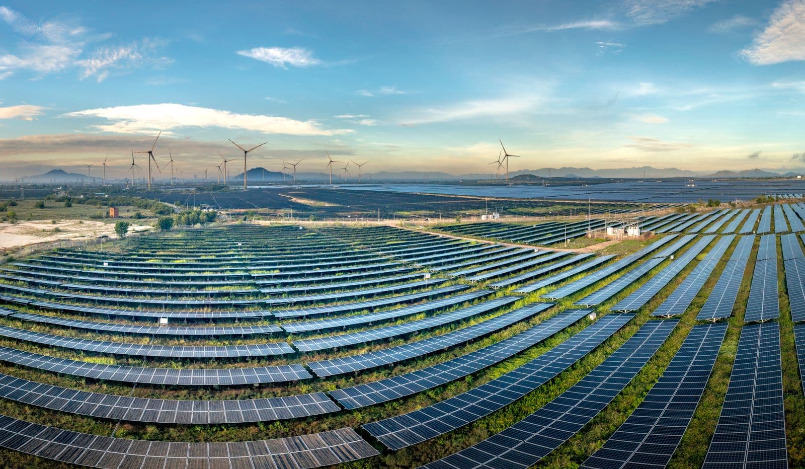 Rows of solar panels with wind turbines on the horizon